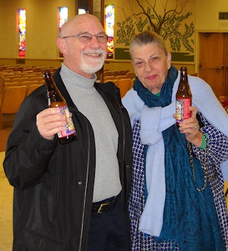 A man and woman smiling and holding up a bottle of kosher beer.
